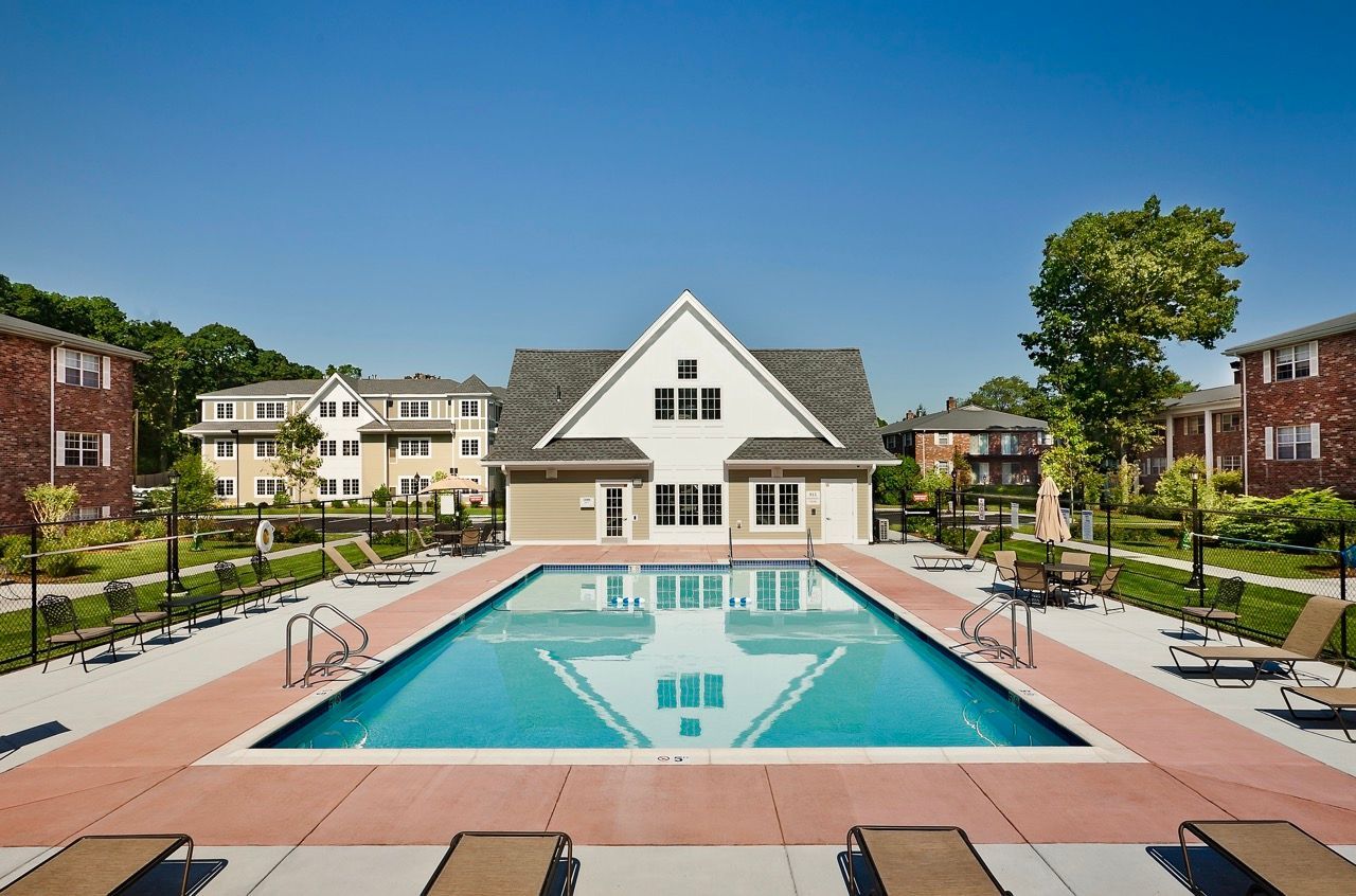 Outdoor communal pool with lounge chairs and a clubhouse at an apartment complex.