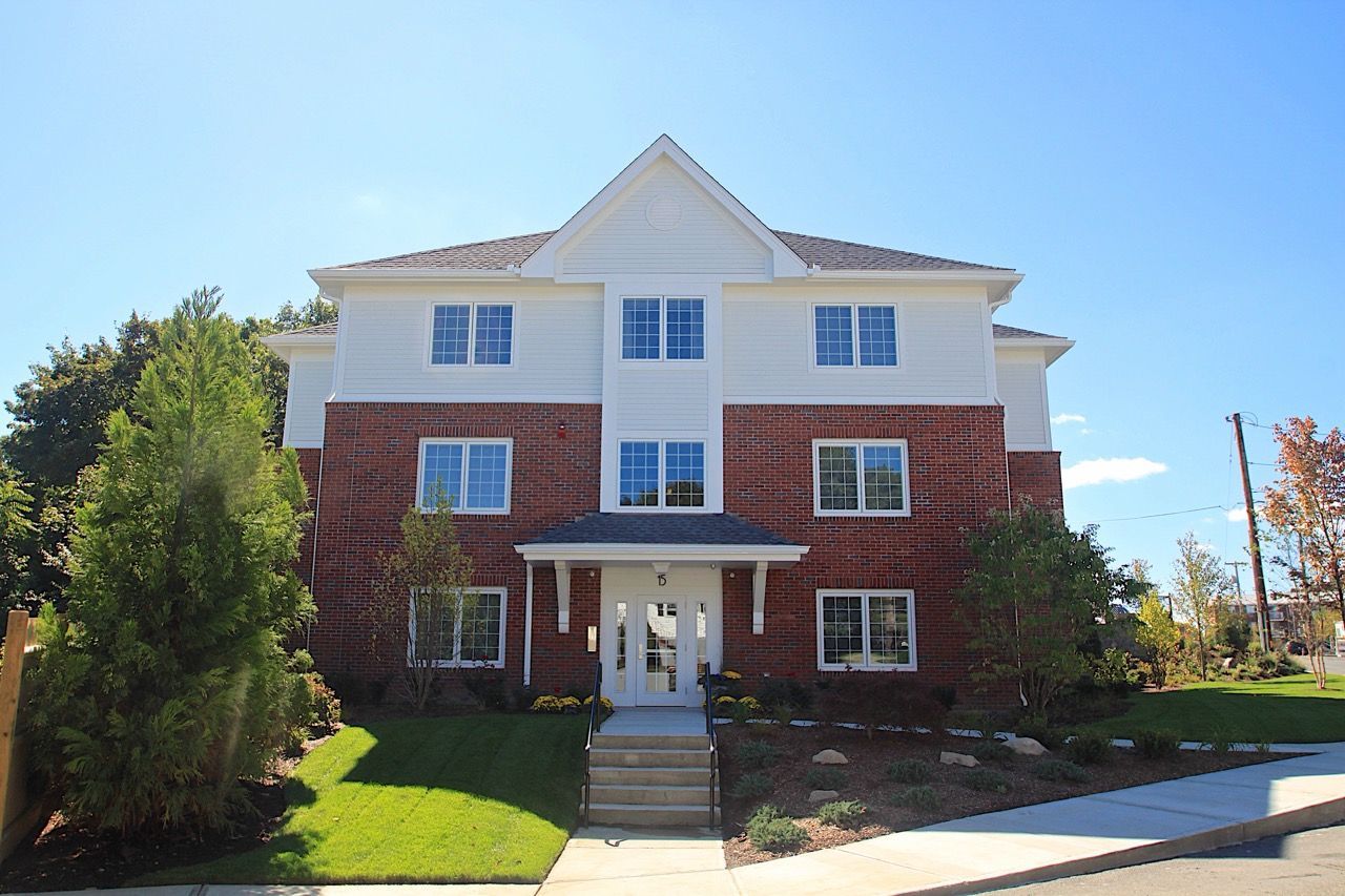 Exterior view of a brick-and-white multifamily building with a front entrance and landscaped lawn.