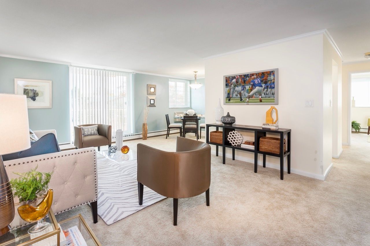 Bright living room with blue accent wall, beige carpet, seating area, and a wall-mounted TV.