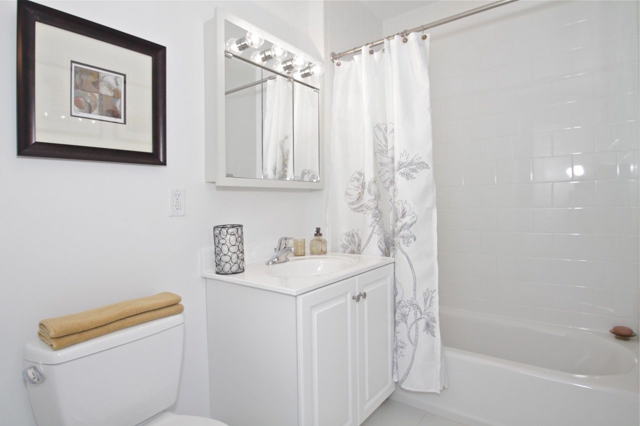 White bathroom with vanity, framed art, toilet, and tub/shower with floral curtain.