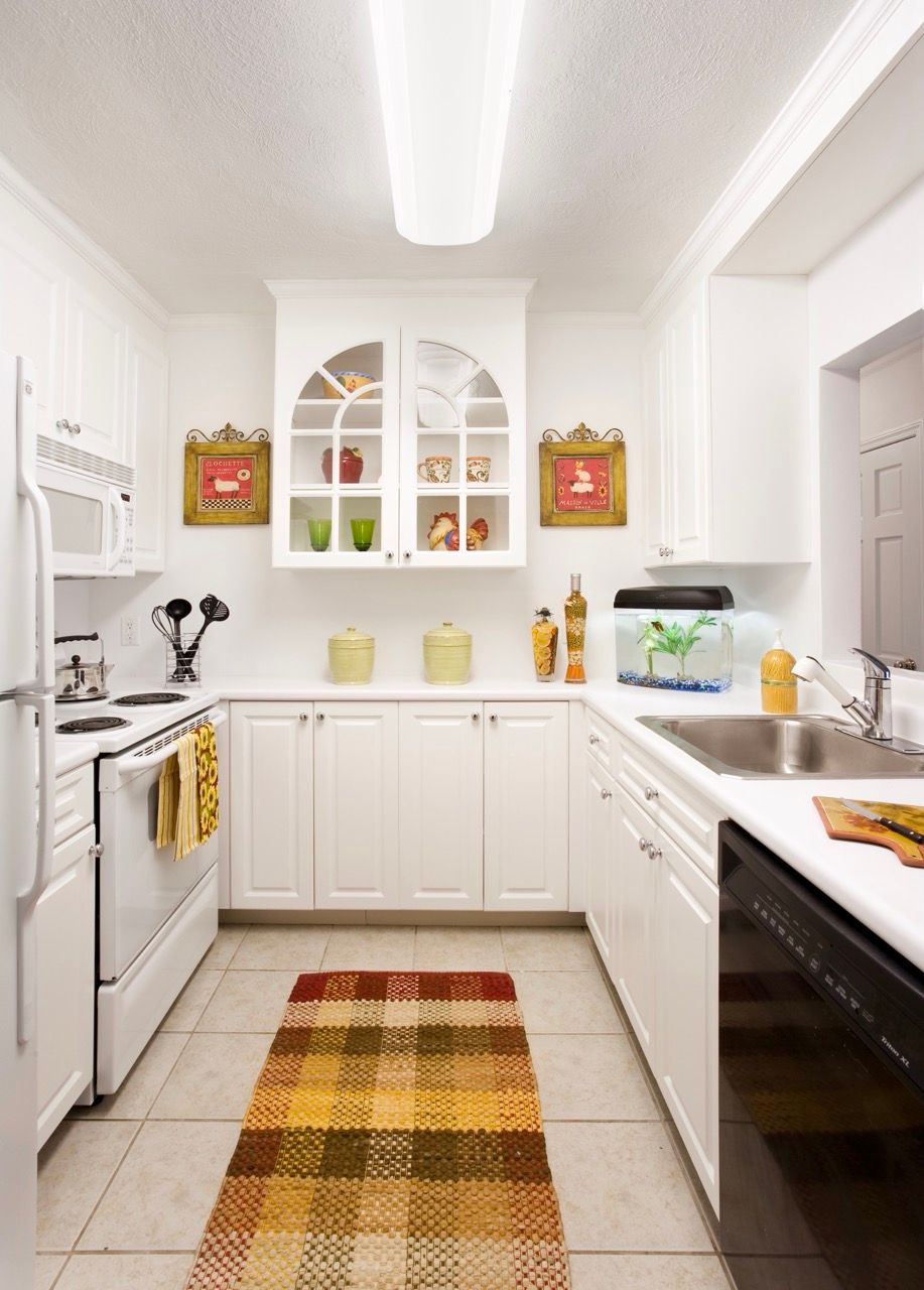 Bright white kitchen with cabinets, stove, sink, and a patterned rug.