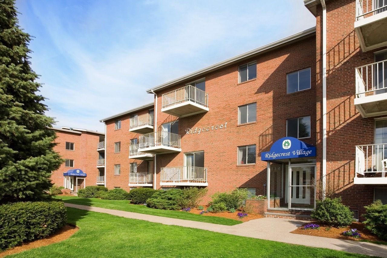 Exterior view of a brick apartment building with balconies and landscaped lawn.