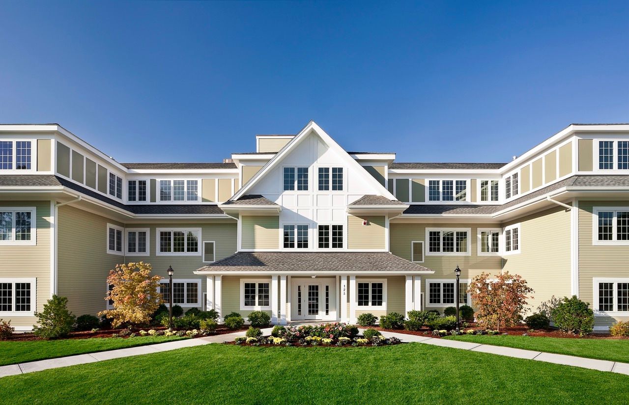 Front exterior view of a beige apartment building with white trim and manicured landscaping.