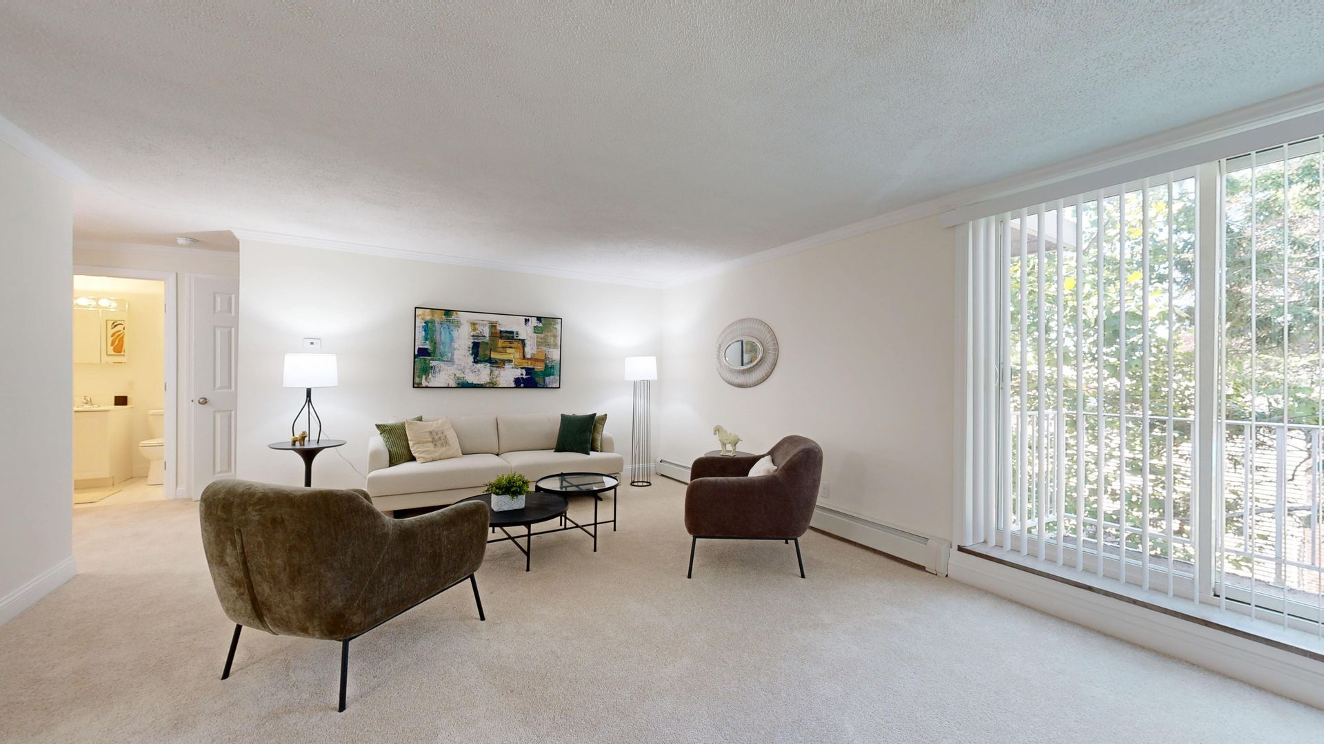 Bright living room with beige carpet, brown chairs, dining table, wall art, and large window blinds