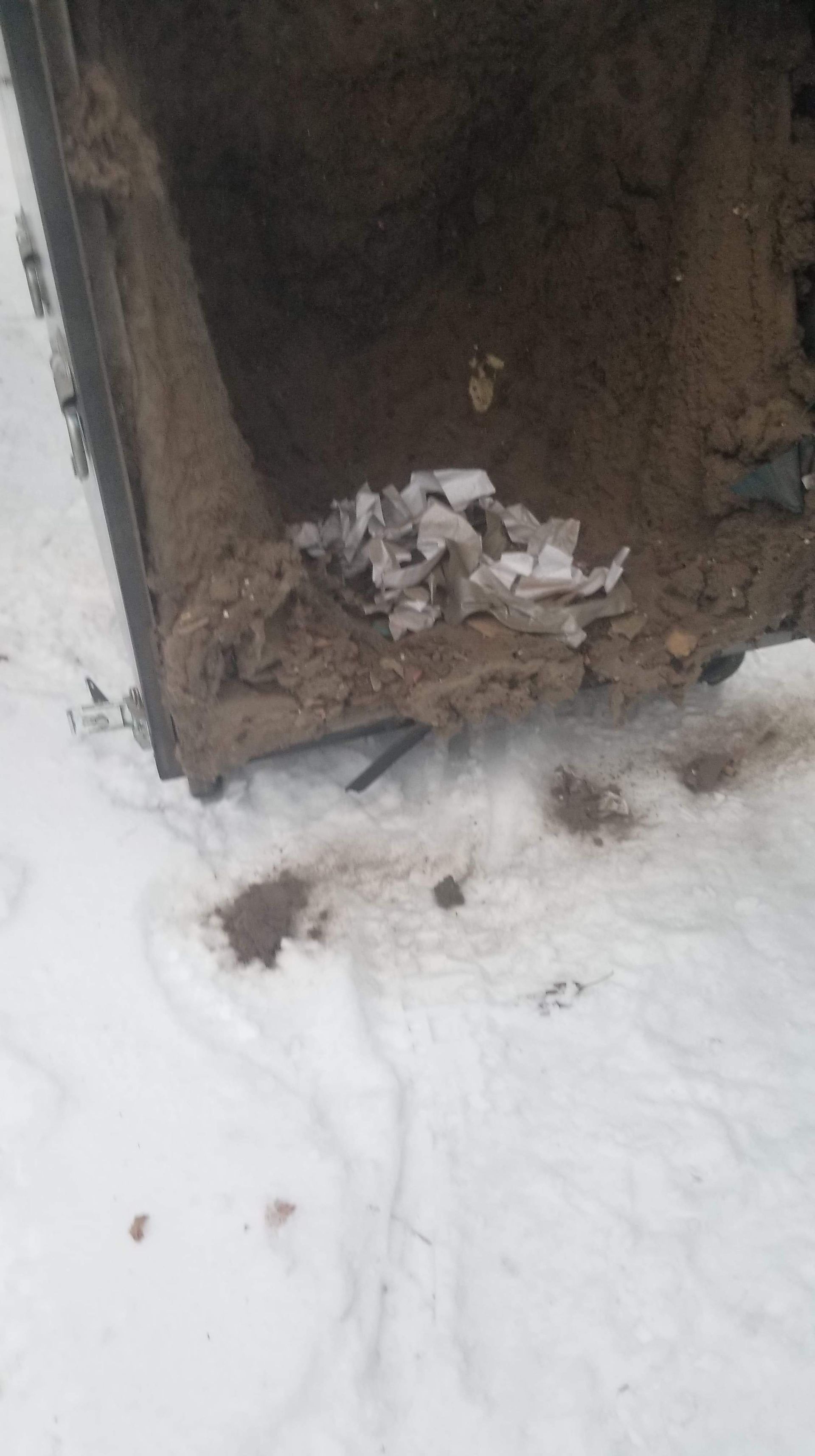 A dirty trash can is sitting in the snow on the ground.