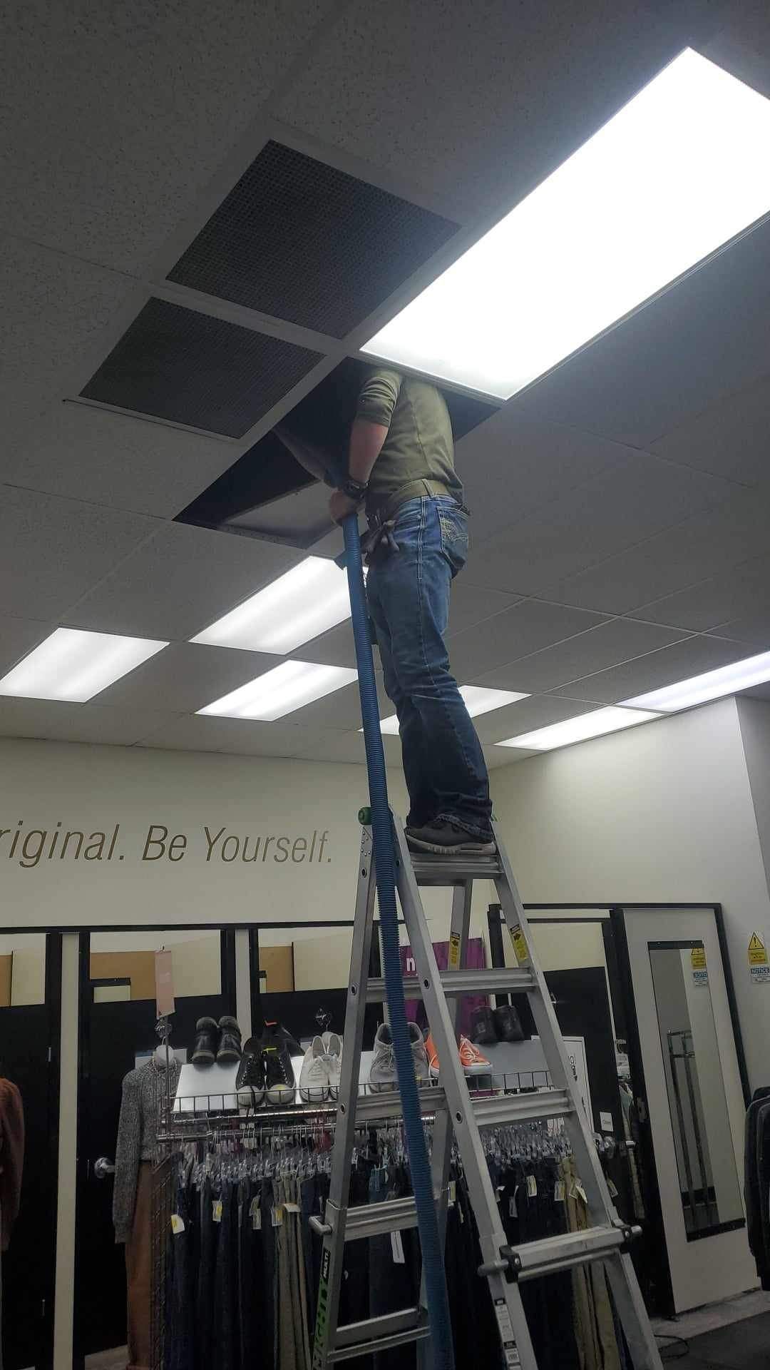 A man is standing on a ladder in a store looking up at the ceiling.