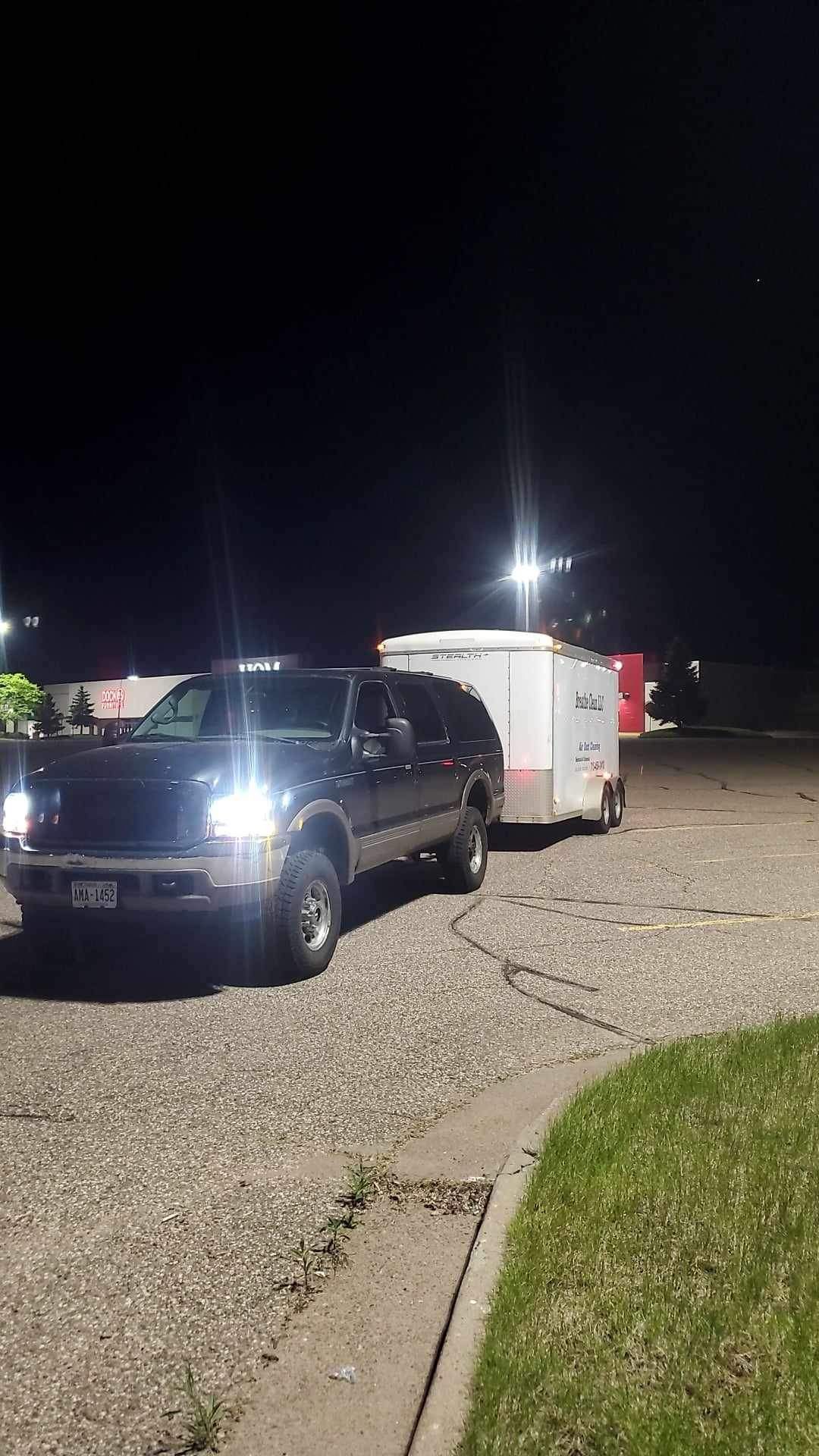 A black suv is towing a white trailer in a parking lot at night.