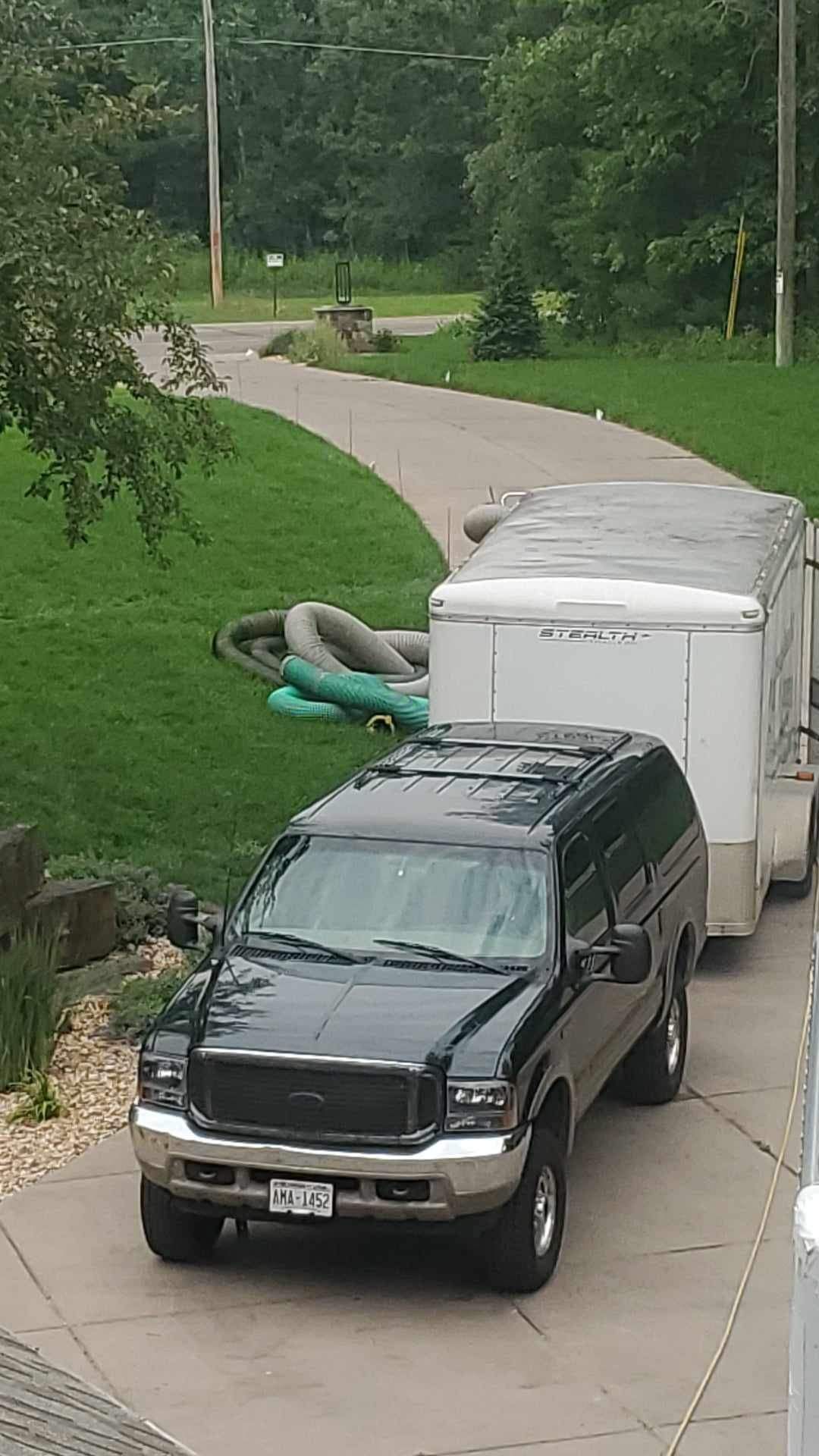 A black suv is parked in a driveway next to a white trailer.