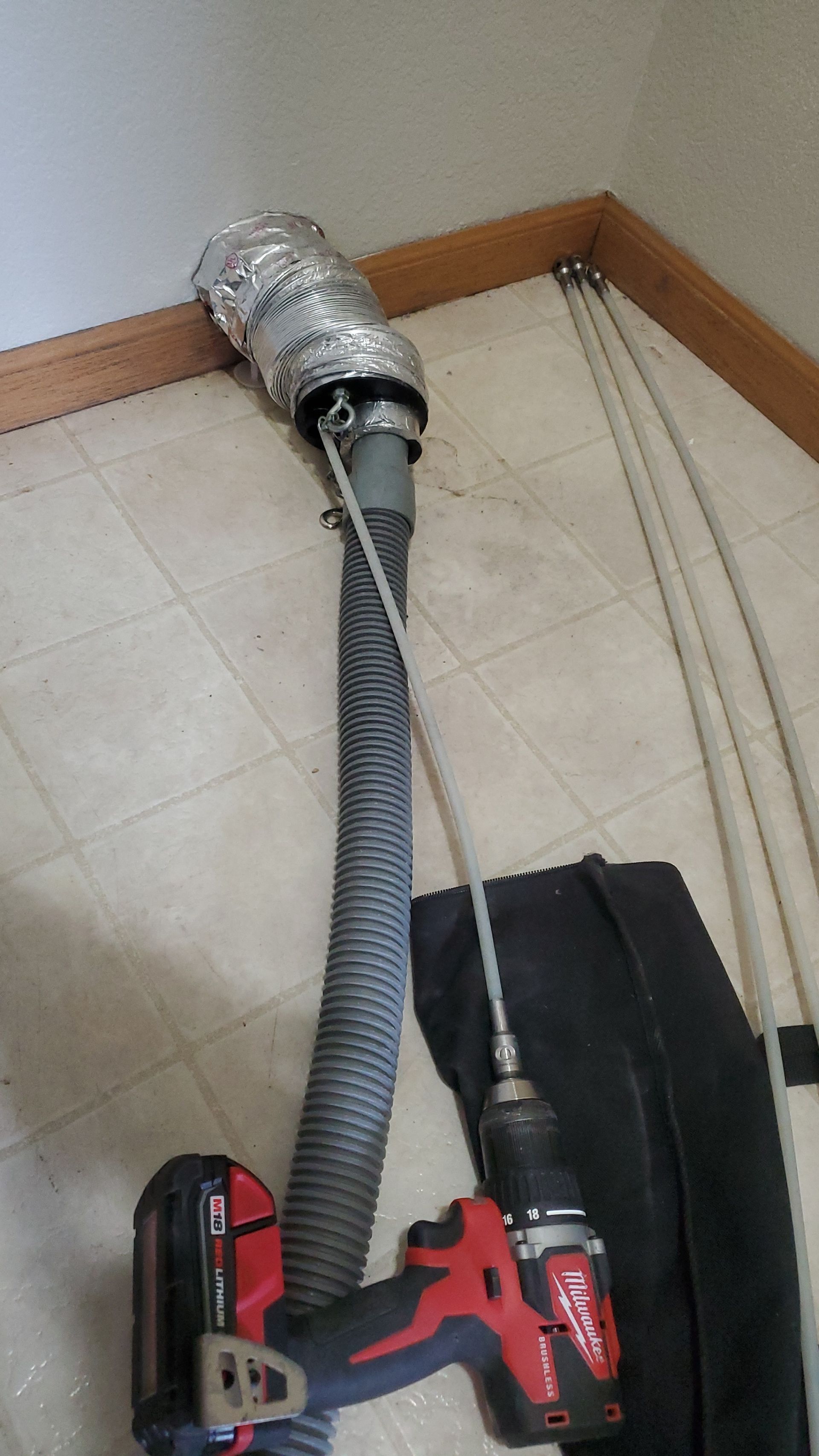 A drill is sitting next to a hose on the floor.