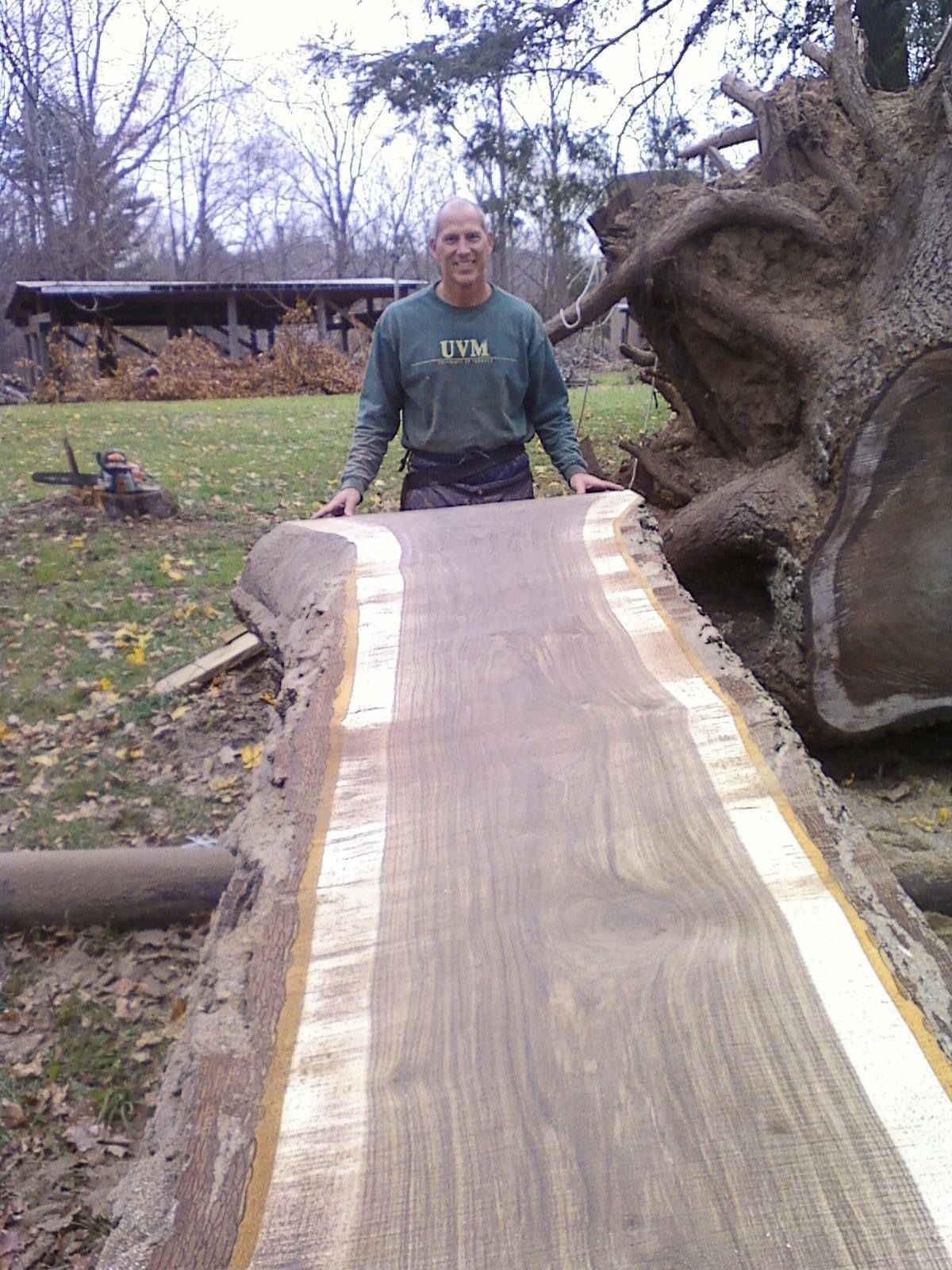 a man wearing an uvm shirt stands next to a large piece of wood