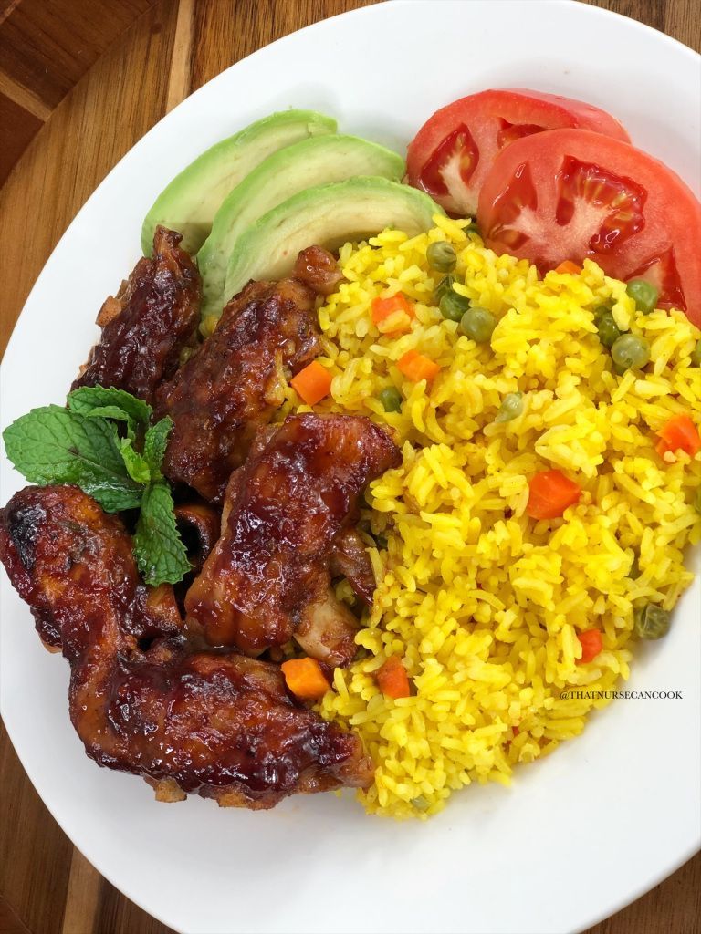 Plate of glazed chicken wings, yellow rice, avocado slices, and tomato.