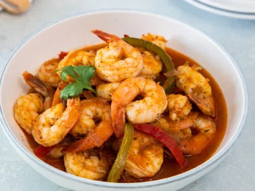 Bowl of cooked shrimp with red and green peppers in a sauce, garnished with cilantro.