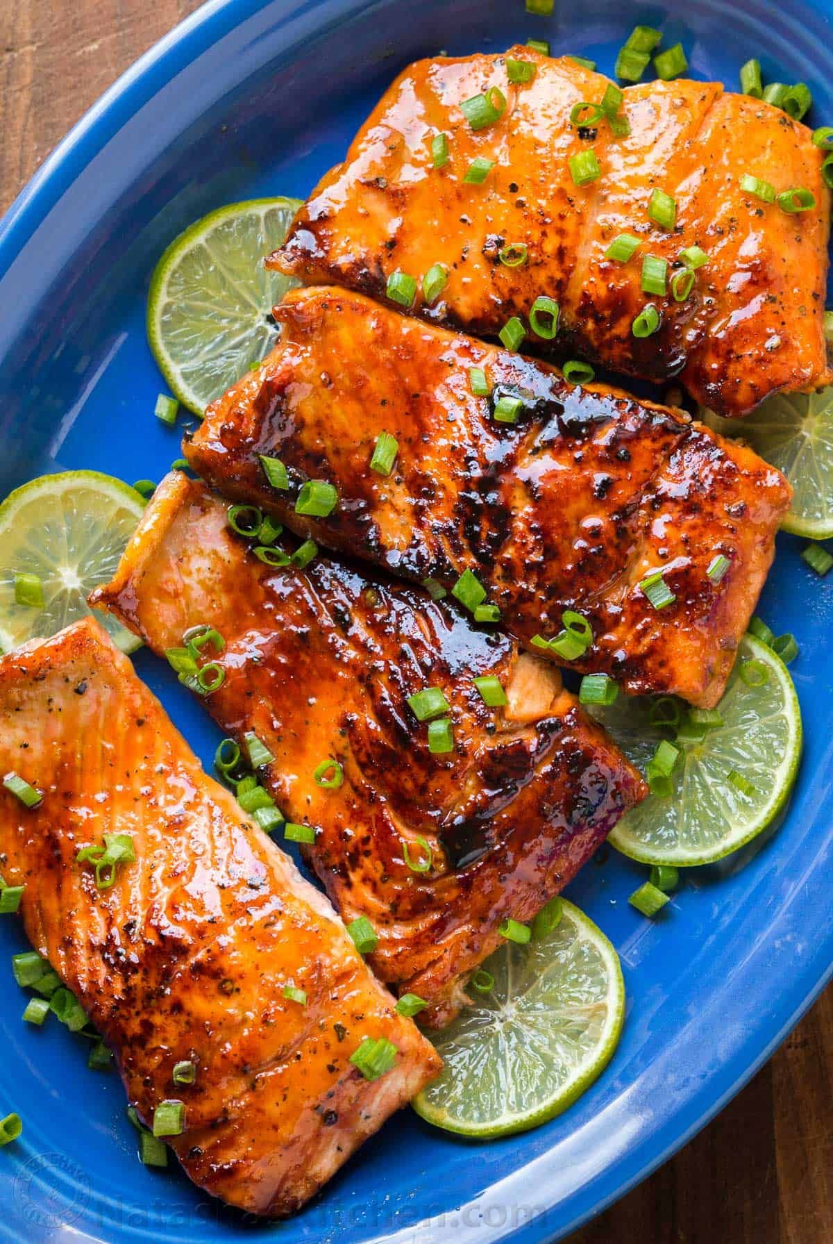 Grilled salmon fillets on lime slices, garnished with green onions on a blue plate.
