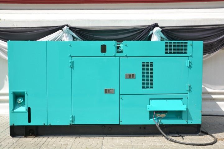 turquoise enclosed generator installed outdoors near a commercial building.