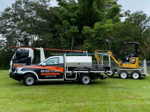 A Truck With A Trailer Attached To It Is Parked In A Grassy Field — River2Coast Concreting in Boambee, NSW
