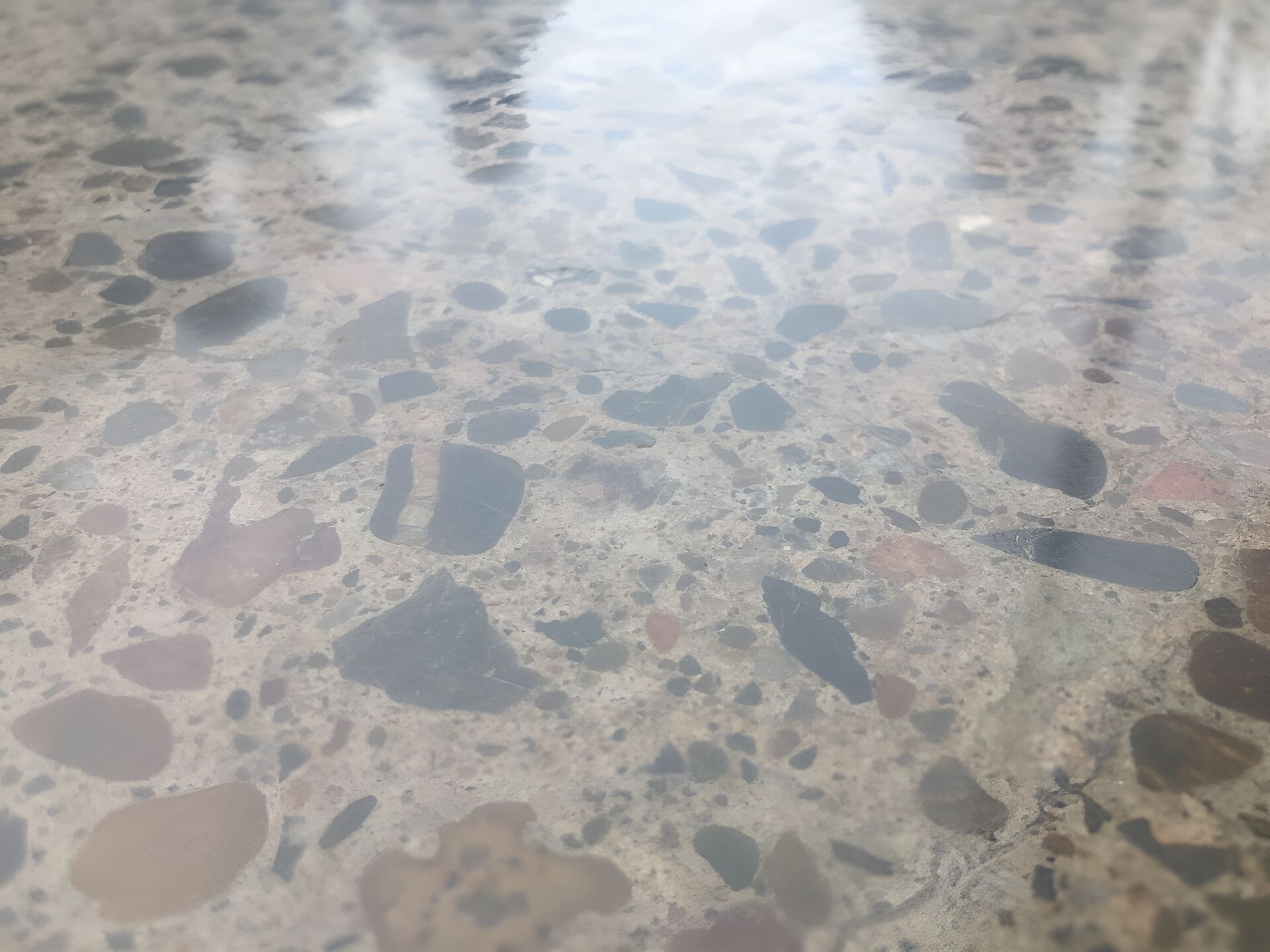 A Close Up Of A Shiny Concrete Floor With A Lot Of Rocks On It — River2Coast Concreting in Boambee, NSW