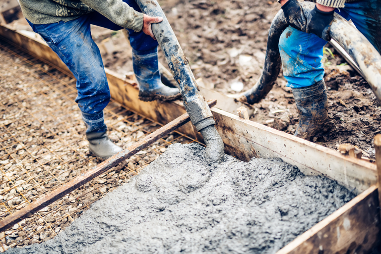 A Couple Of Men Are Pouring Concrete Into A Hole In The Ground — River2Coast Concreting in Boambee, NSW