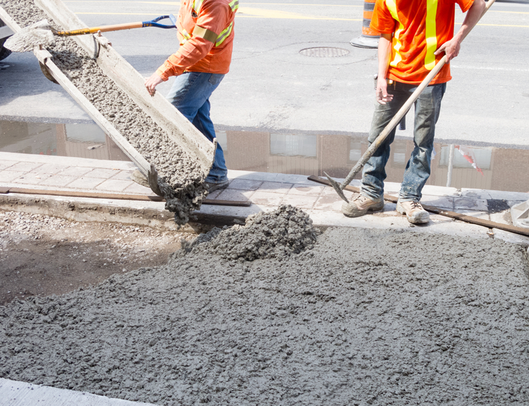 Two Construction Workers Are Pouring Concrete On A Sidewalk — River2Coast Concreting in Boambee, NSW