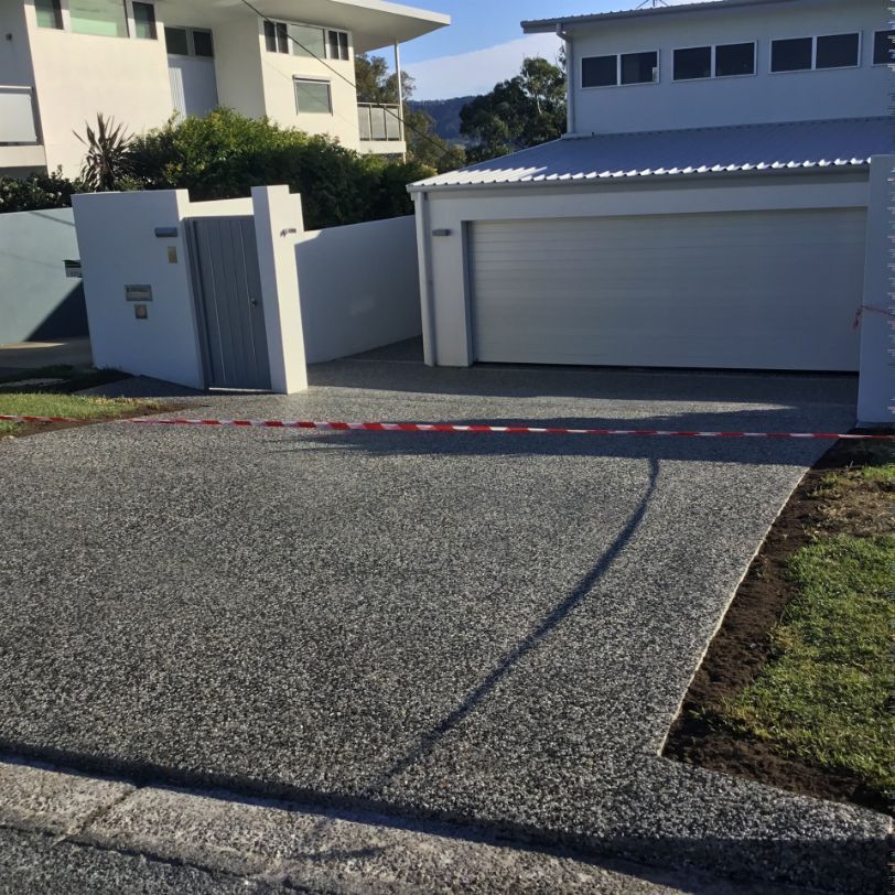 A Driveway Leading To A House With A White Garage Door — River2Coast Concreting in Boambee, NSW
