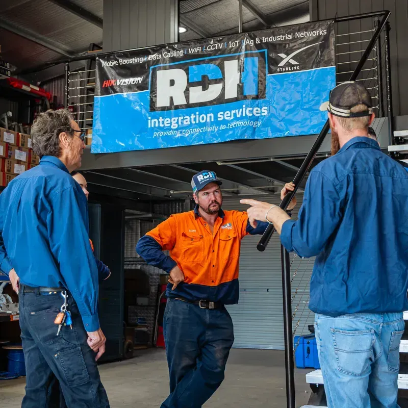 Three men are standing in a warehouse discussing a project.