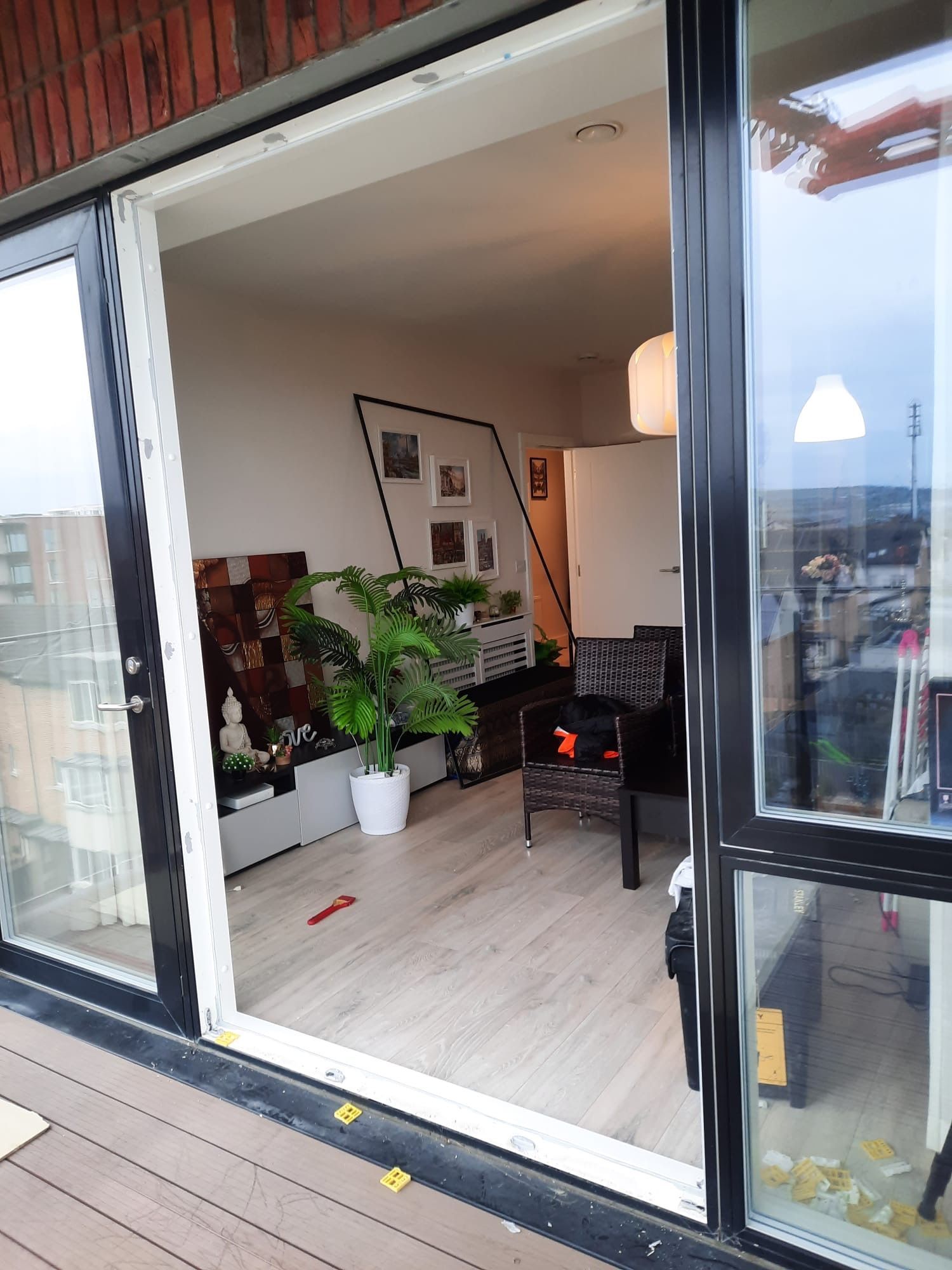 Balcony doorway opening to a cozy living room with plants, chair, and lamp on a wooden deck