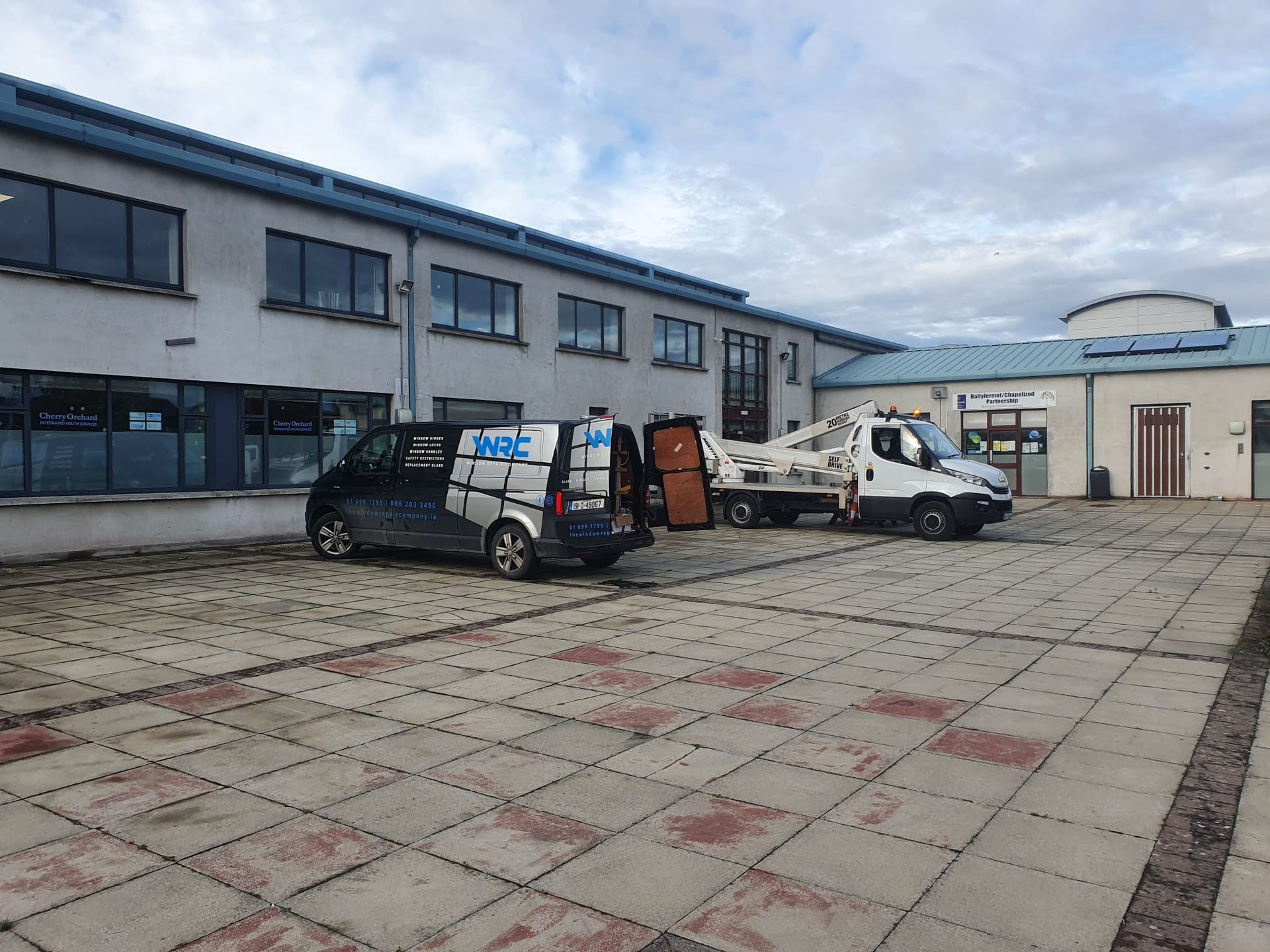 Industrial courtyard with two vans parked beside a gray warehouse under a cloudy sky