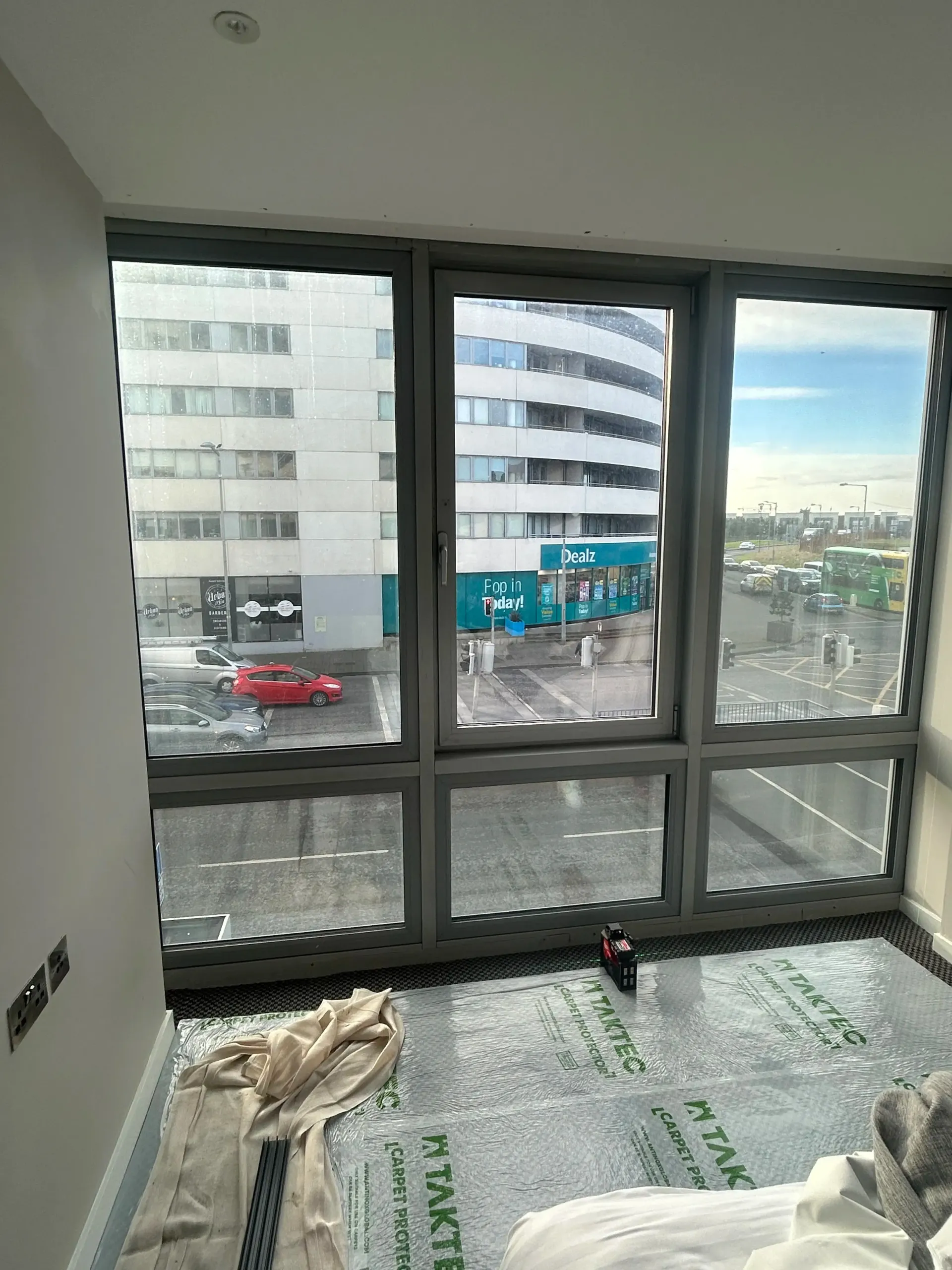 Empty room with large windows overlooking a city street and buildings.