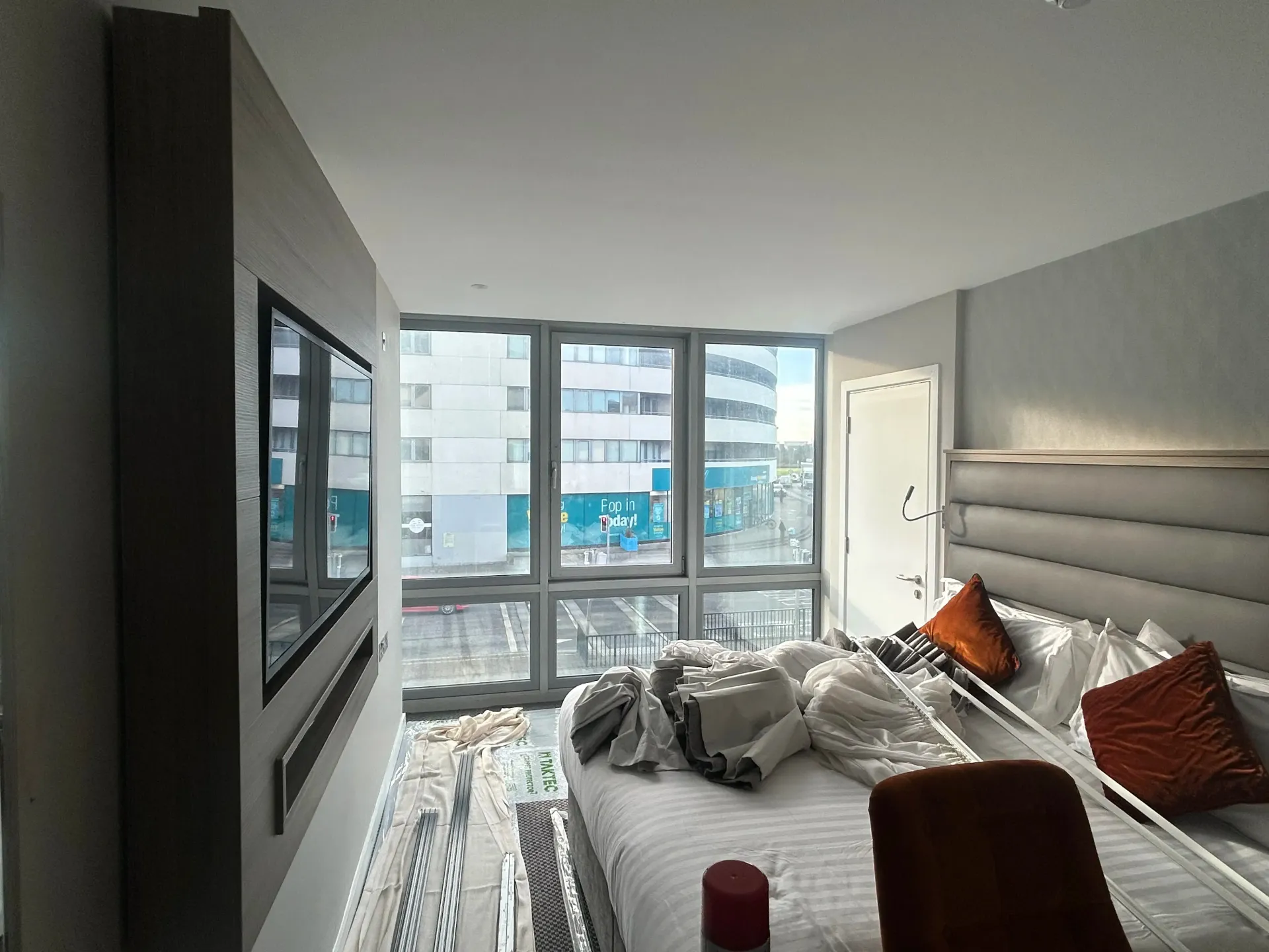 Modern bedroom with a large window, white bed, gray walls, and city buildings outside