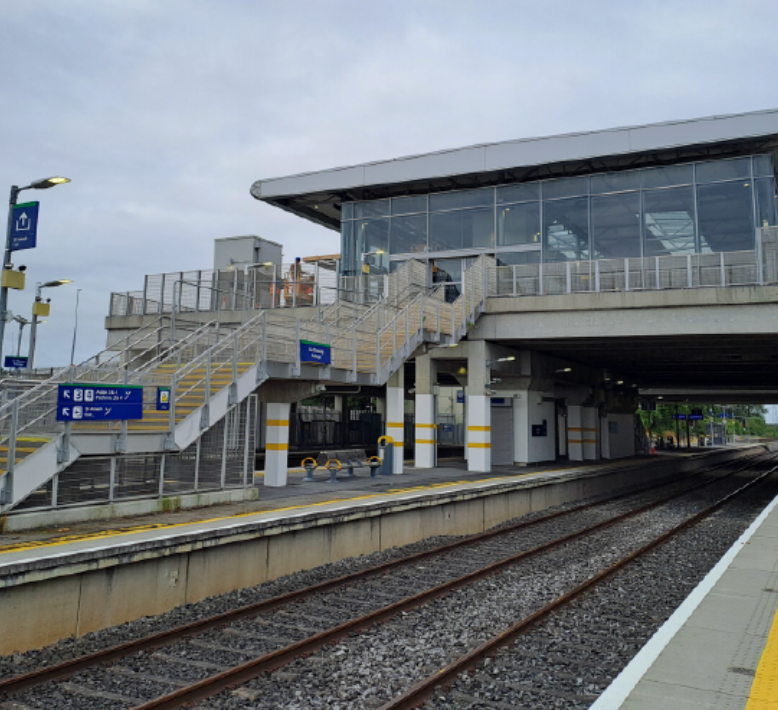 Empty train station platform with stairs, glass waiting area, and tracks on an overcast day