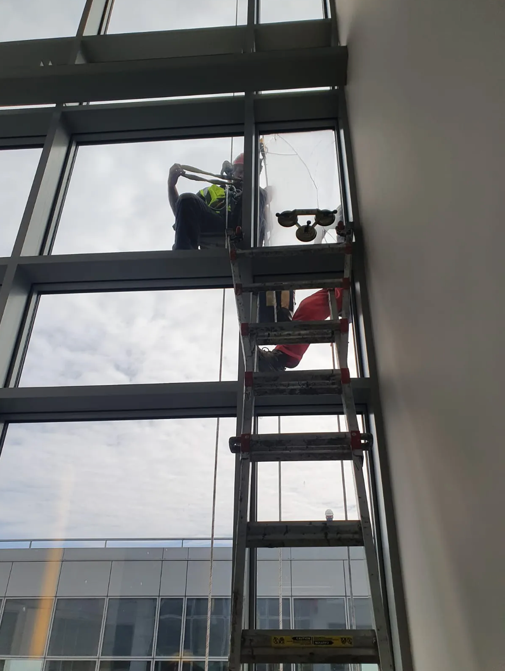 Worker on a ladder repairing a tall window inside a building lobby