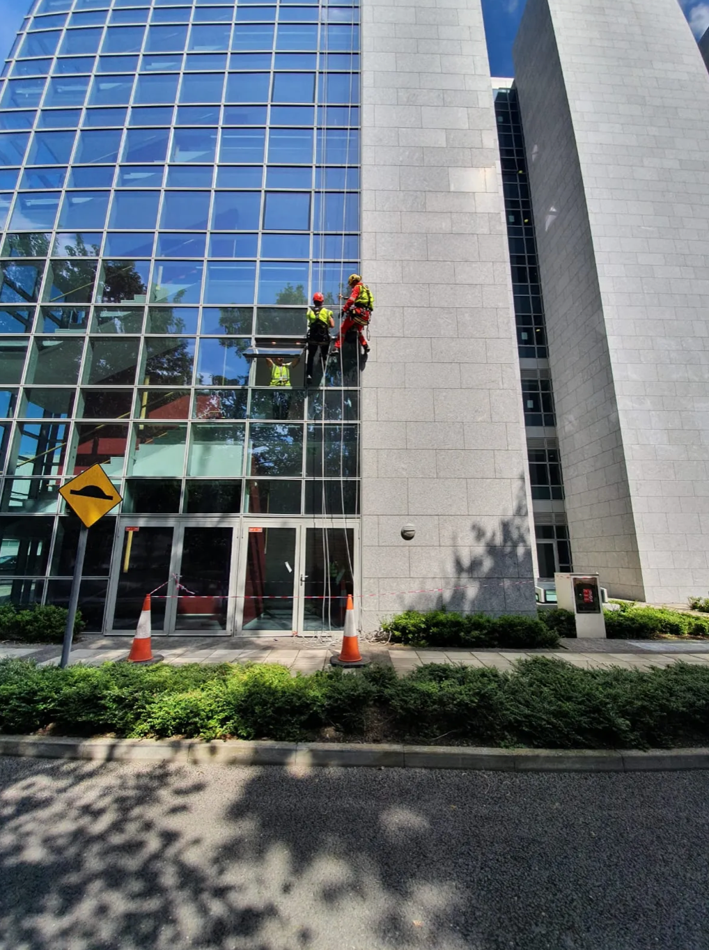 Workers on a rope access job cleaning a glass office building beside a street.