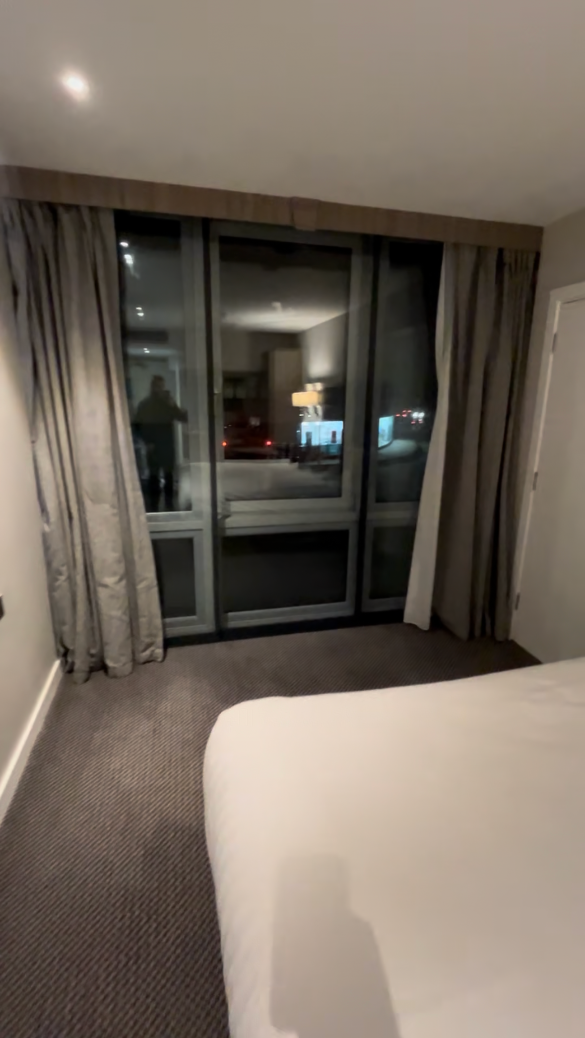 Hotel room with bed and curtains framing a glass door to a balcony at night.