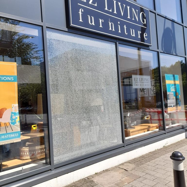 Storefront with large frosted window and signage for “Living Furniture” on a sunny street.