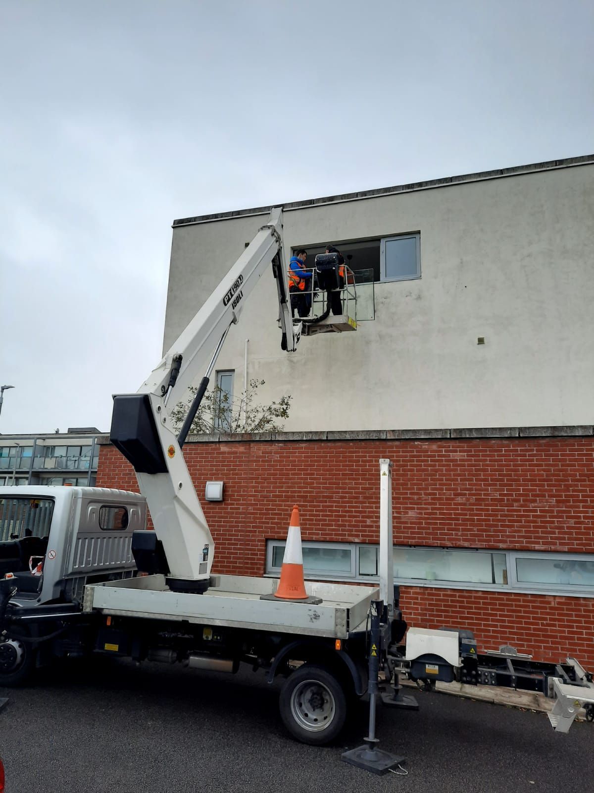Utility truck lift basket raising workers to a window on a brick building wall