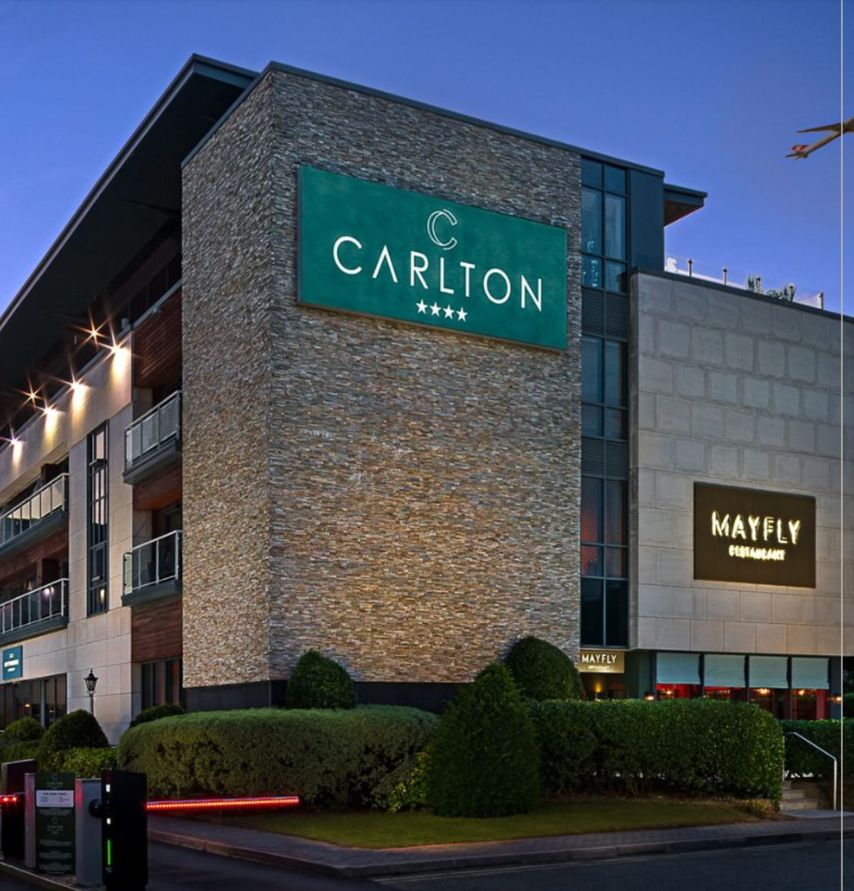 Exterior of Carlton Hotel at dusk, with stone facade and illuminated signs in green and gold.