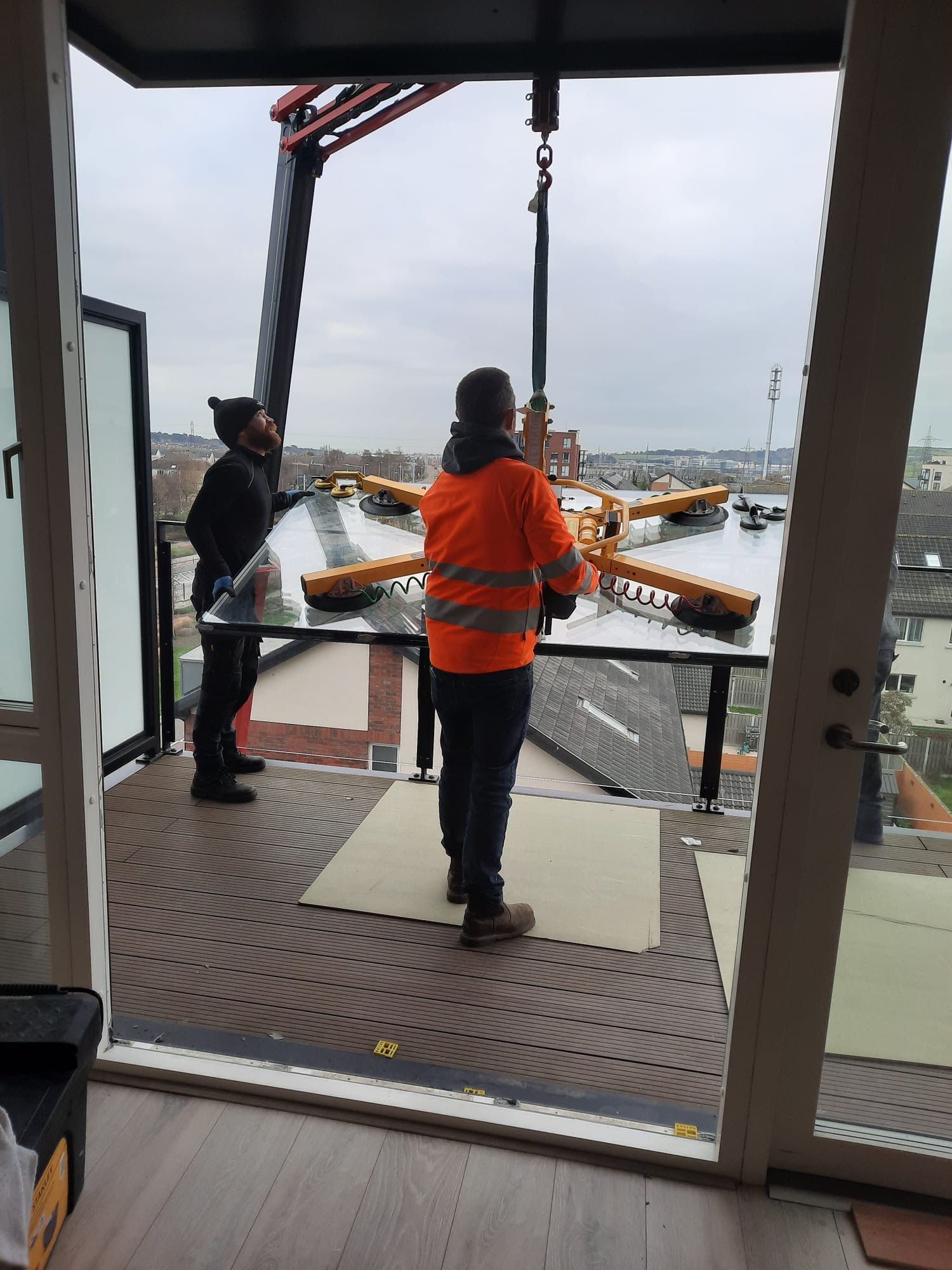 Two workers in orange safety gear stand on a dock, guiding equipment over the water.