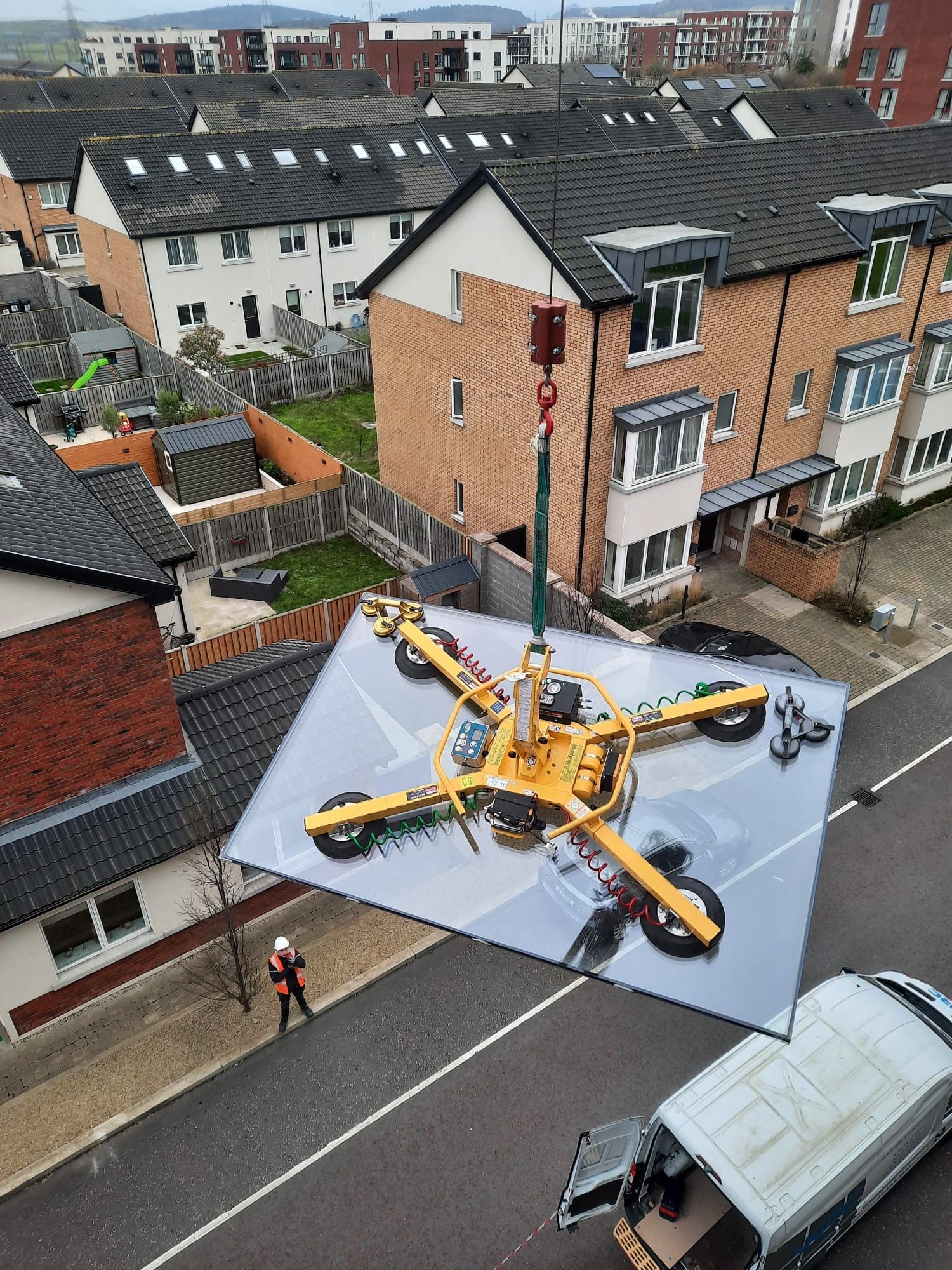 Yellow construction helicopter hoisting a large roof panel over a street of houses