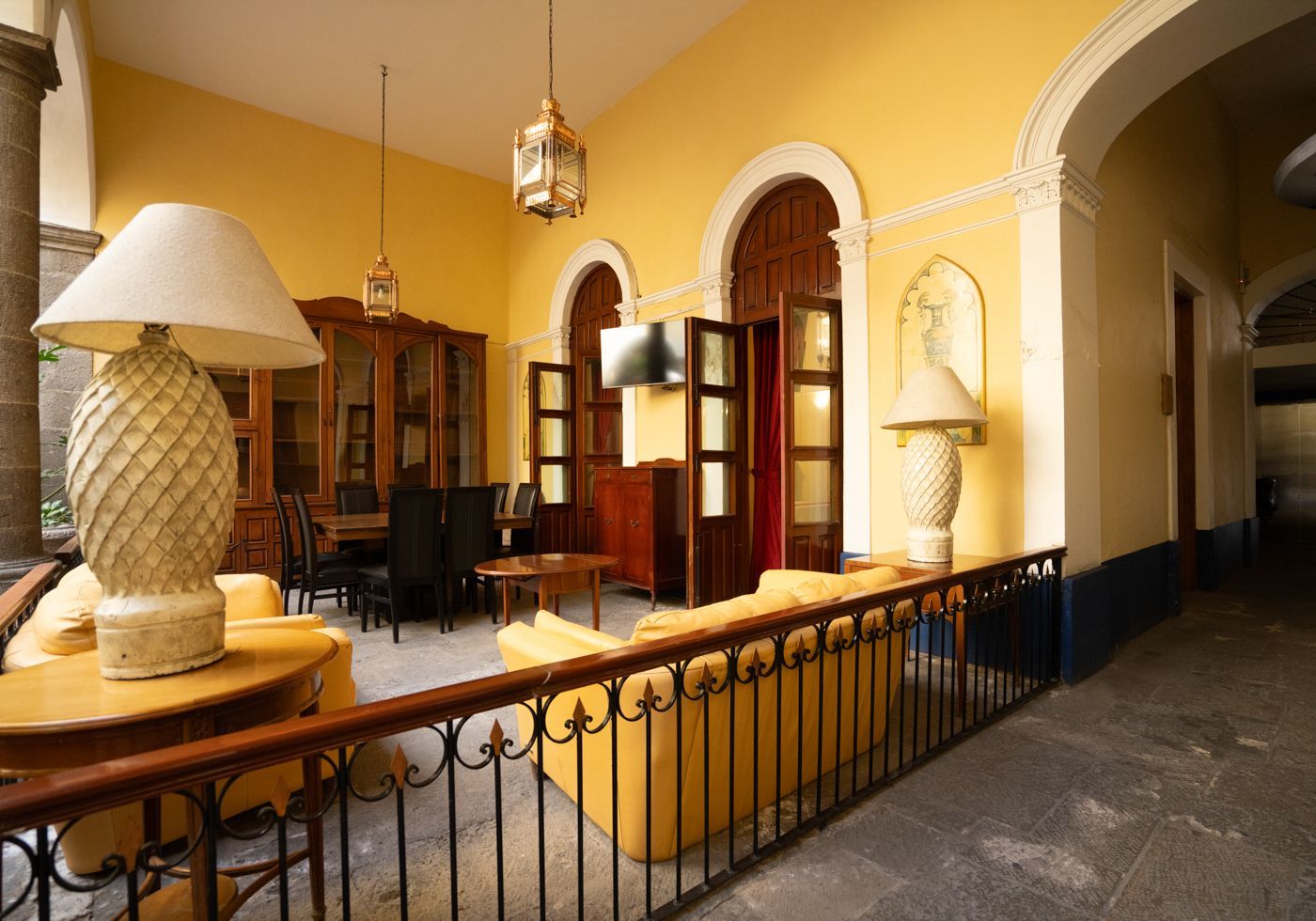 Patio amarillo cálido con puertas en arco, barandilla de hierro forjado y lámparas en un pasillo interior alicatado