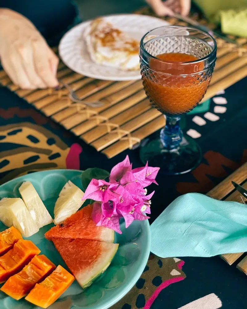 Uma cena vibrante de café da manhã com um prato de frutas fatiadas, um copo de suco de laranja e uma porção de comida sobre uma esteira de bambu.