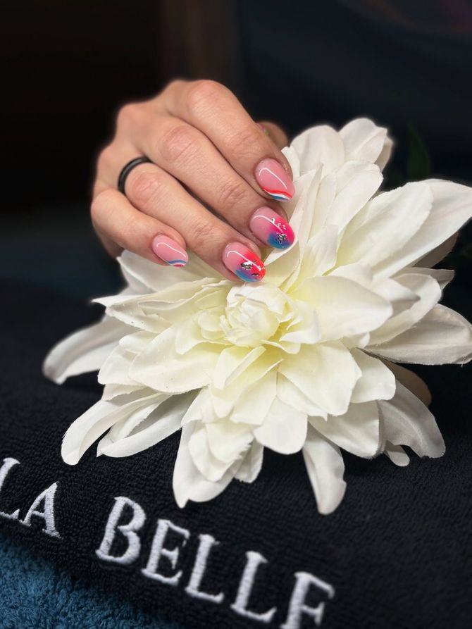 Una mano con unghie rosa decorate con fiori che tiene un fiore bianco sopra una maglietta nera LA BELLE.