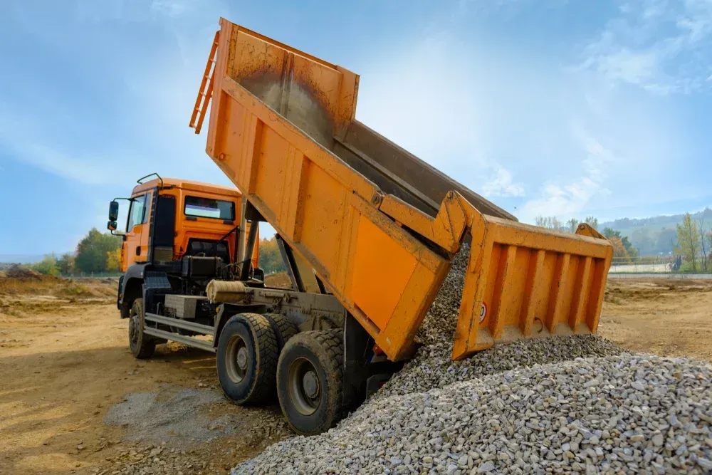 Orange dump truck unloading gravel at a construction site, with a raised bed spilling rocks onto a pile. — Rainman Domestic Water In Bargara, QLD