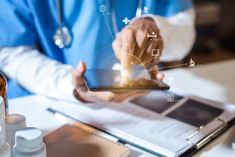 A healthcare professional in a blue uniform uses a tablet with a digital interface overlay of various medical icons.