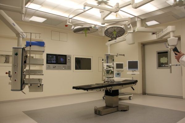 An empty, modern surgical operating room featuring a surgical table, ceiling-mounted lights, and medical equipment.