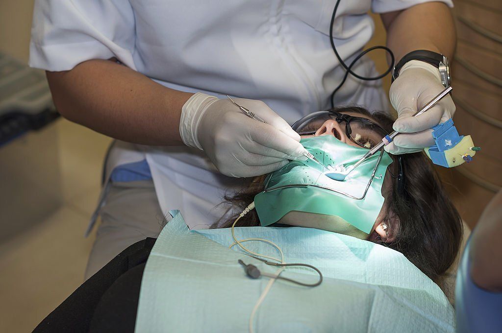 A dentist in white scrubs and gloves performs a procedure on a patient wearing a green dental dam and bib.