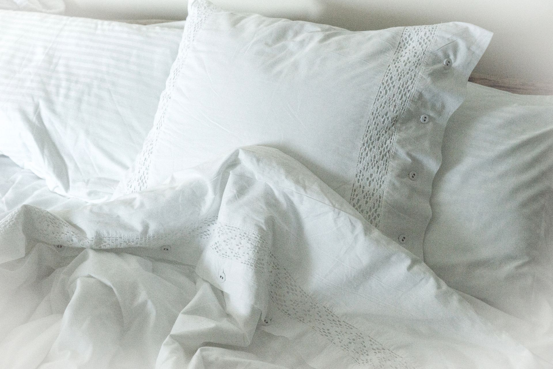 Primer plano de una cama blanca con almohadas con volantes y una manta texturizada, que crean un ambiente suave y acogedor.