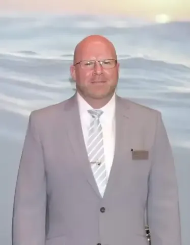 A man in a suit and tie is standing in front of a painting of the ocean.