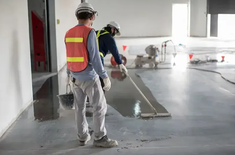 Two construction workers smoothing wet gray concrete on a floor indoors