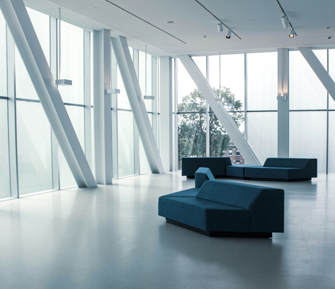 Minimalist modern lobby with blue sofas, white floors, and large angled glass windows