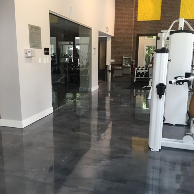 Gym interior with glossy gray floor, exercise machines, and a glass-walled room.