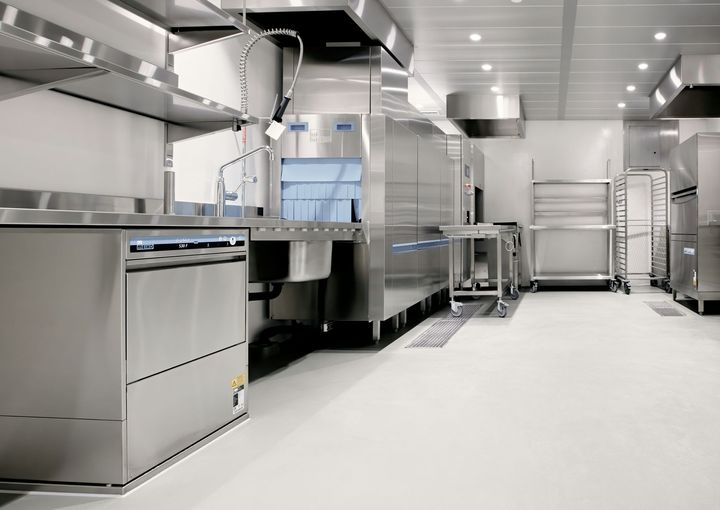 Modern stainless-steel commercial kitchen with ovens, prep counters, and bright white floor